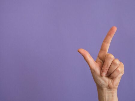 Hand with two fingers raised on purple background and copy spaceの写真素材