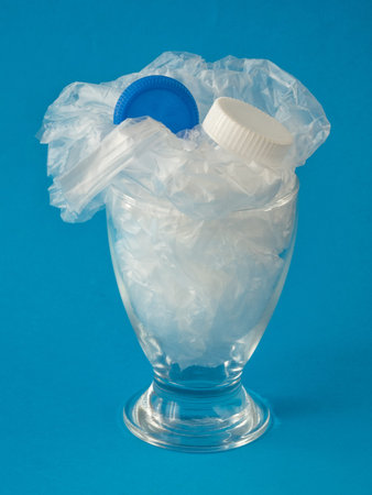 Glass with plastic inside on blue background - drinking plastic environmental concept