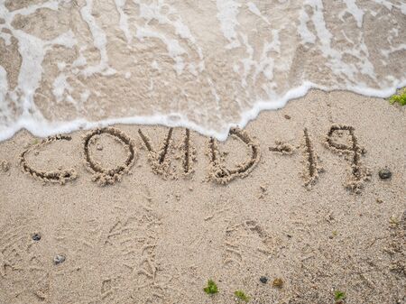 COVID-19 written in the sand and a sea waveの写真素材