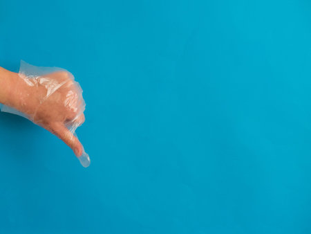 Hand with plastic glove with thumb down on blue