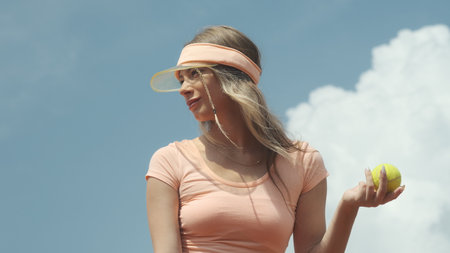 The girl on the background of the sky holds a yellow tennis ball in her handsの写真素材
