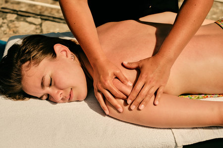 Under the sun, on the beach, a female masseuse massages the muscles of a girl's left armの写真素材