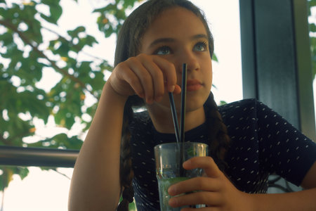 A young girl is sitting at a table in a summer cafÃ©, drinking a drink and thinkingの写真素材