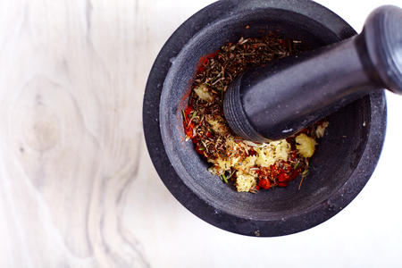 Garlic, paprika coriander seeds and other spices in a mortar. On white wooden background.の写真素材