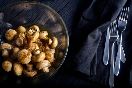 Roasted mushrooms in bowl with onions and white whine vinegar and spices on dark wood background with forks on napkins near itの写真素材