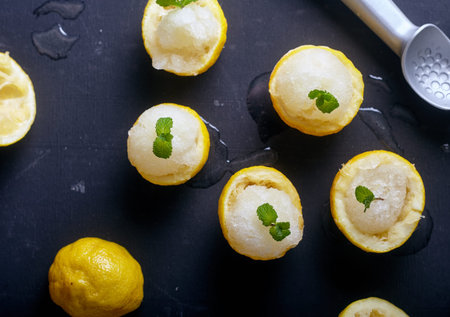 Top view of lemon sorbet or ice cream inside fresh lemons decorated with mint leaves. Dark wood background with ice cream spoon on backの写真素材