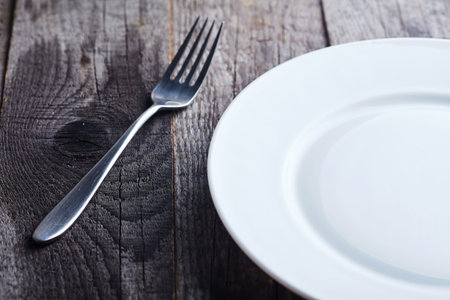 Metal fork and white plate on a wooden surface, closeup
