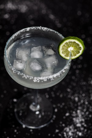 Classic mexican margarita cocktail on black background. Margarita glass full of ice, salt and lime on side. Black background with whites sea salt spots.の写真素材