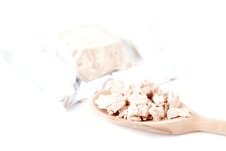 Fesh yeast on wooden spoon. Package of fresh yeast bar on back. Isolated on white image. Yeast is a main ingredient of fresh bread dough, pizza dough and many other dough's.の写真素材