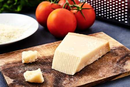 Piece of parmigiano reggiano cheese and grated parmesan cheese on wood board on stone background....