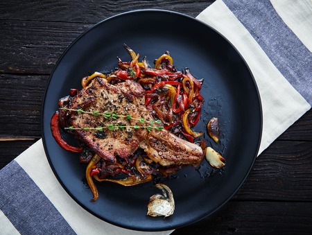 Delicious, juicy, hot club steak veal on the bone. Meat Prime rib with sauteed bell peppers and onions, decorated with two sprigs of thyme on a black plate with a toasted bun and garlic. Main dishの写真素材