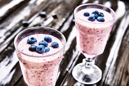 Two beautiful vintage glasses filled healthy blueberry smoothies with fresh berries and yogurt on dark wooden blurred background. Tasty, organic food for diet breakfast and healthy lifestyle. Close-upの写真素材