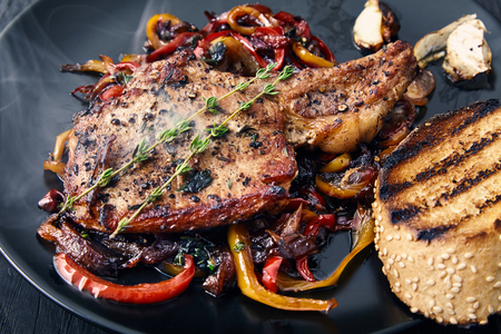 Delicious, juicy, hot club steak veal on the bone. Meat Prime rib with sauteed bell peppers and onions, decorated with two sprigs of thyme on a black plate with a toasted bun and garlic. Main dishの写真素材