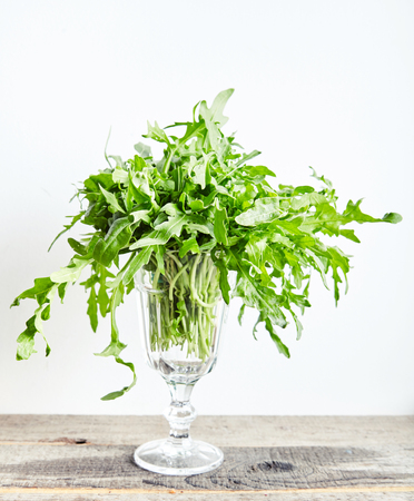 Bunch fresh arugula or rucola or rocket salad leaves at glass on wooden table. Arugula is rich in vitamins and trace elements. Perfect for salads, meat dishes, pasta or sauce pesto. Green foodの写真素材