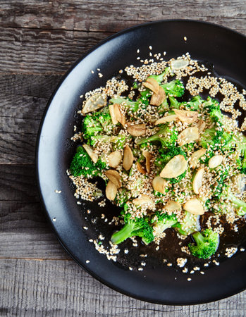 Close-up view of delicious steamed broccoli with garlic chips sprinkled with sesame seeds and dressed with soy sauce and ginger on the black plate.の写真素材