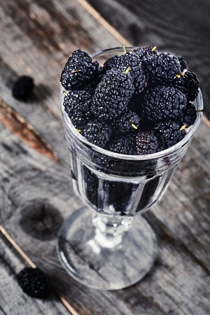 Sweet and sour fresh organic ripe mulberries in wine glass on wooden background.の写真素材