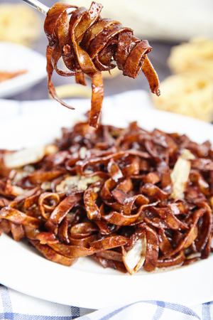 Tasty egg noodles with bacon bits and fried Chinese cabbage in a sauce of soy sauce and spices on white plate. Part of pasta on fork. Fettuccine nest on the background. Close-up, selective focusの写真素材