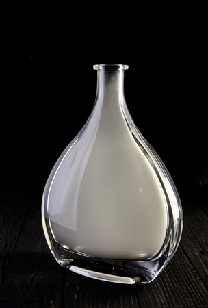 Empty glass liquid decanter graceful shape on a black wooden background with smoke in it. Crystal pitcher for alcohol in directional light. Isolatedの写真素材