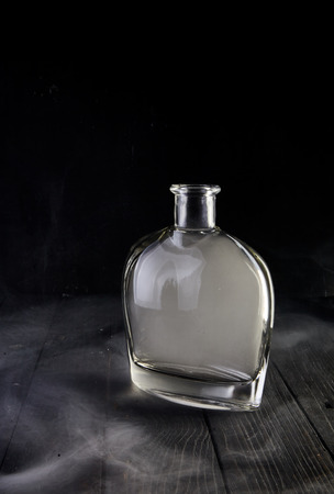 Empty glass liquid decanter graceful shape on a black wooden background with smoke in it. Crystal pitcher for alcohol in directional light. Isolatedの写真素材