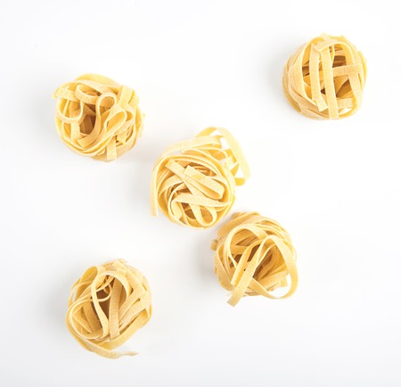 Uncooked rolled traditional italian pasta on white background, isolated. Portion of raw fettuccine or tagliatelle or pappardelle. Dry pasta from whole wheat flour. Ingredients for tasty dishの写真素材
