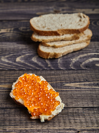 Delicious sandwich with butter and red salmon caviar on stack of wheat bread on wood background. Traditional Russian appetizer. Selective focus, rustic styleの写真素材