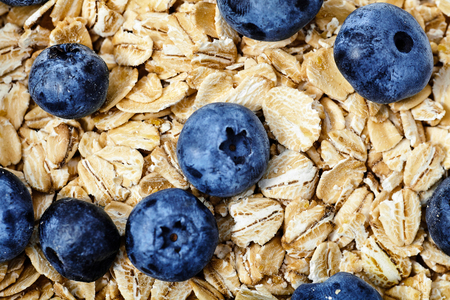 Macro shot of raw oat flakes topped fresh blueberries in white bowl.の写真素材