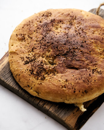 Homemade focaccia lying on a wooden board. The top of the focaccia is sprinkled with oregano,...