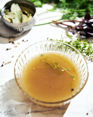 Vegetable stock in glass bowl. Ingredients of stock on the background
