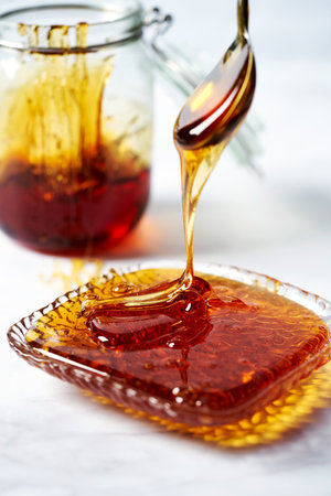 Thick golden syrup or caramel or honey dripping from the spoon into the plate. White background.の写真素材