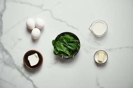 Iingredients for healthy spinach and feta omelette. Eggs with heavy cream, Fresh baby spinach leaves in the black ceramic bowl, white marble background. Top view food photoの写真素材