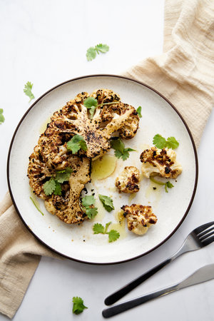 Baked cauliflower steak on white plate with cilantro leavesの写真素材