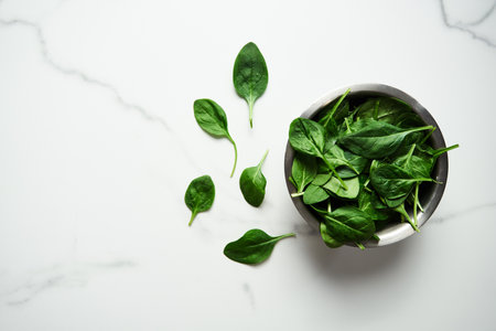 A bunch of Fresh baby spinach leaves in the in a stainless steel bowl on white marble background.Flat lay, top view with copy spaceの写真素材
