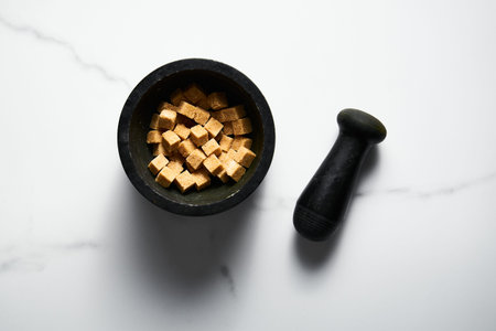 Brown sugar cubes in in a pail on white marble background.
