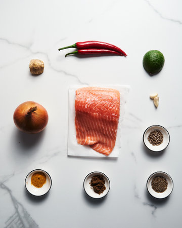 Indian salmon curry ingredients on white marble background. Salmon fillet with spices like garam masala, coriander with garlic and chilli. Tomatoes used for tomato sauce and red color. Top viewの写真素材