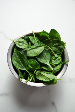 A bunch of Fresh baby spinach leaves in the in a stainless steel bowl on white marble background.の写真素材