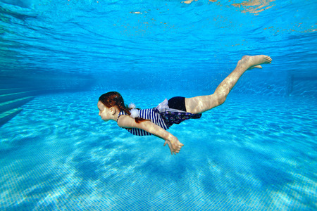 Happy little girl in striped swimsuit swimming underwater in pool on blue background.の写真素材