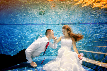 The groom kisses the hand of the bride underwater in the pool. Portrait. Shooting under water. Landscape orientationの写真素材