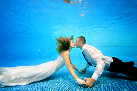 The bride and groom in wedding dresses kissing underwater at the bottom of the pool. Horizontal view. Shooting under waterの写真素材