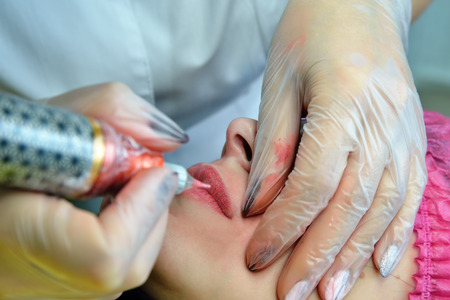 On the lips of the young woman applied pink paint to the needle during the procedure of permanent lip makeup. Extremely close-up. Shallow depth of field. Horizontal orientation of the image.の写真素材