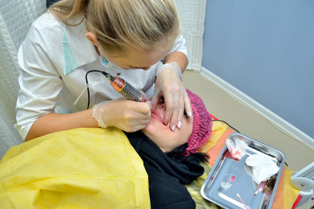 A cosmetologist in a white medical gown makes a European woman permanent lip makeup in a beauty...