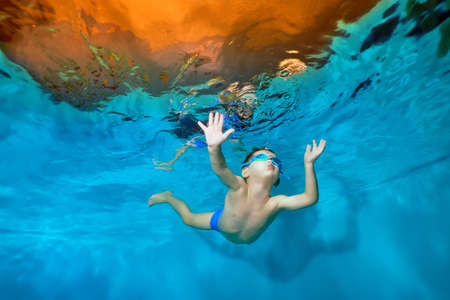 A little boy is floating underwater in the pool with his arms outstretched. Dancing underwater. Creative. Portrait. Underwater photography. Horizontal orientation of the image.の写真素材