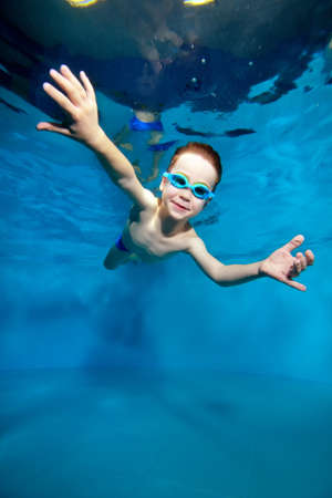 A small sports a boy he was smiling is sailing under's surface water. Creative. Posing with open eyes. Portrait. Underwater photography. Vertical orientation of the image.の写真素材