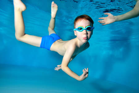 A happy little boy goes in for sports and swims underwater in the pool with his arms outstretched. Portrait. Close up. Underwater photography. Horizontal orientation.の写真素材