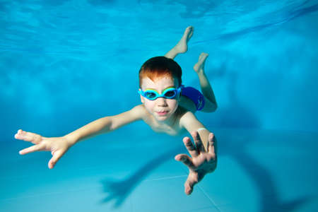 Cute sports boy swimming underwater in the pool. Posing for the camera with glasses. Bottom view from the bottom of the pool. Portrait. Underwater photography. Horizontal view.の写真素材