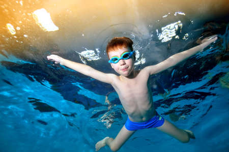 A little boy swims and plays underwater in the pool with his hands spread apart and looks at the camera. Portrait. Underwater photography. Horizontal orientation of the image.の写真素材