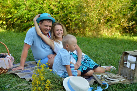 Happy family. Picnic in nature on a summer day. Mom and dad in a woman's hat, smiling look at his little son in nature. Portrait. Horizontal view.の写真素材