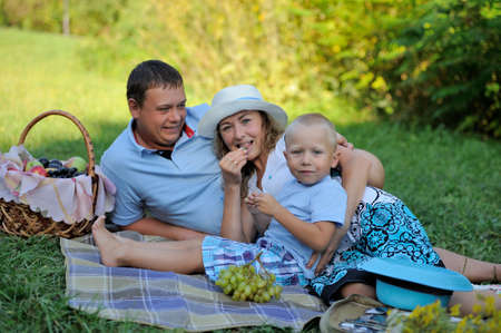 A picnic, a happy family. Mom, dad and baby on the beach with a basket of fruits and flowers. Smiling at the camera. Portrait. Horizontal view.の写真素材
