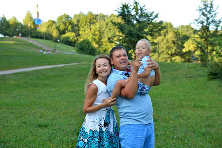Family with a child walking in the Park at sunset summer day. Baby sitting in the arms of his father. Dad points his hand to his son on something. The concept of family happiness. Portrait.の写真素材