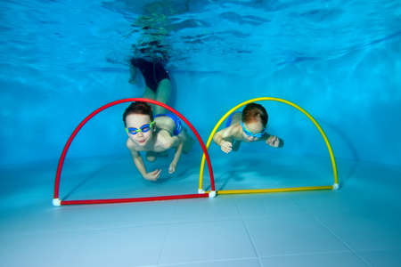 Two young athletic boy swimmers underwater. Frolic and swim through the colored hoops. View from the bottom of the pool. Portrait. Underwater photography. Horizontal view.の写真素材