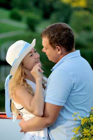 Lovers guy and girl hugging and gently looking at each other in the Park by the water at the sunset of the summer day. Girl white hat. Nature walk. Portrait. Vertical view.の写真素材